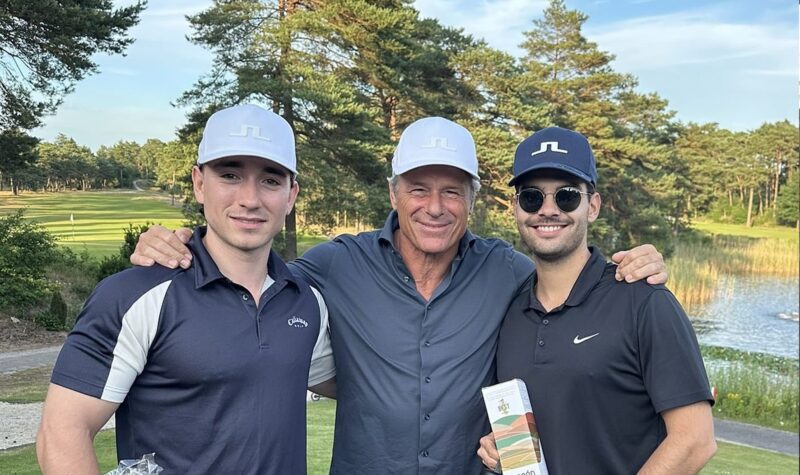 Three smiling men posing together on a golf course