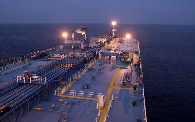 Large oil tanker ship deck illuminated at dusk on ocean